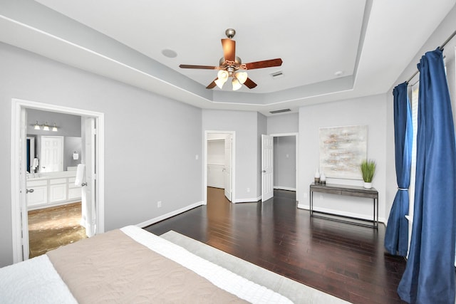 bedroom with ceiling fan, connected bathroom, dark hardwood / wood-style floors, and a raised ceiling