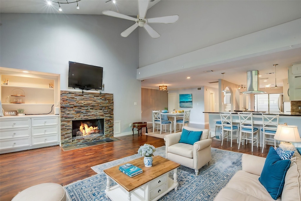 living room featuring dark wood-type flooring, a fireplace, ceiling fan, and vaulted ceiling