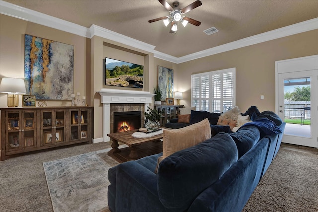 carpeted living room with a tiled fireplace, ceiling fan, crown molding, and a textured ceiling