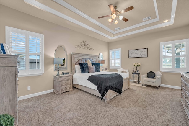 bedroom with light carpet, a tray ceiling, multiple windows, and ornamental molding