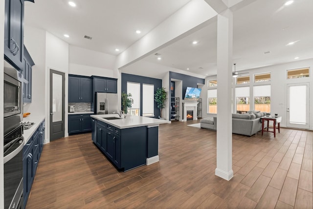 kitchen featuring sink, ceiling fan, stainless steel appliances, an island with sink, and decorative backsplash