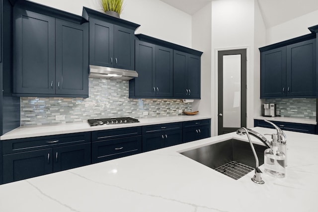 kitchen with tasteful backsplash, gas stovetop, light stone countertops, and sink