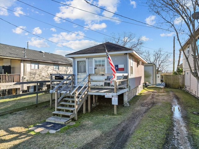 rear view of property featuring driveway, stairway, roof with shingles, fence, and a deck