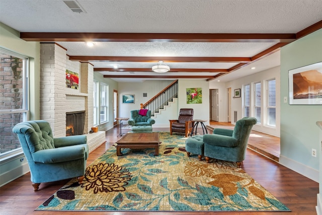 living room featuring a brick fireplace, dark wood-type flooring, a textured ceiling, and beam ceiling