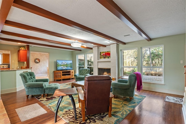 living room featuring beam ceiling, dark wood-type flooring, a textured ceiling, and a fireplace