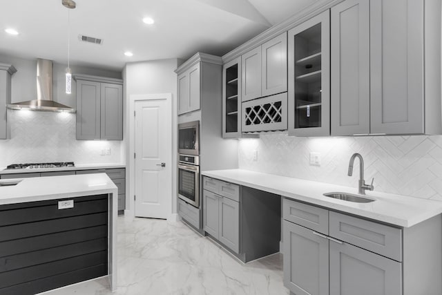 kitchen with wall chimney exhaust hood, sink, hanging light fixtures, appliances with stainless steel finishes, and gray cabinets