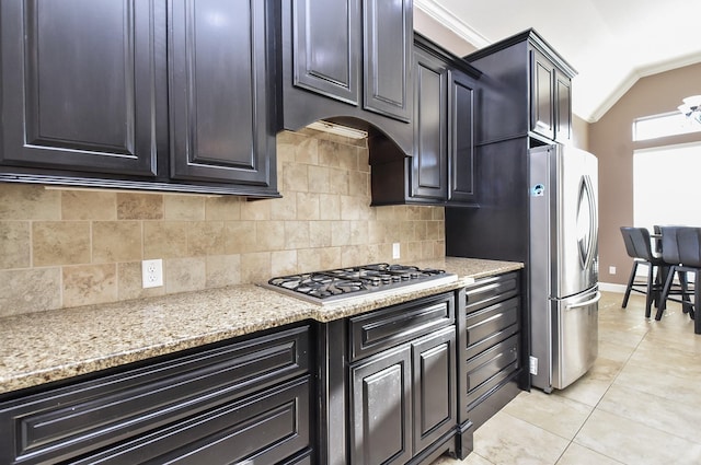 kitchen featuring light stone counters, tasteful backsplash, dark cabinetry, appliances with stainless steel finishes, and light tile patterned floors