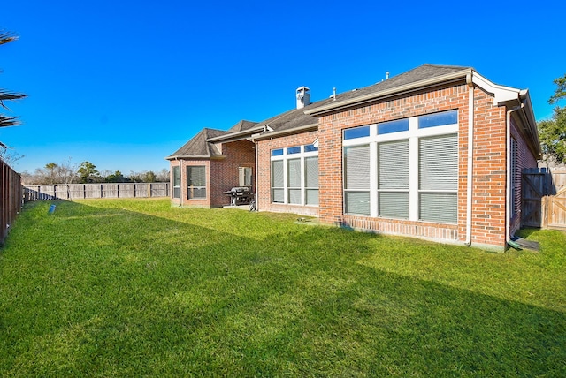 rear view of property featuring brick siding, a fenced backyard, a lawn, and a shingled roof