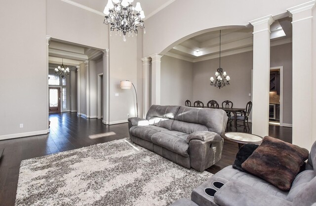 living room with ornate columns, crown molding, dark wood-type flooring, and a chandelier