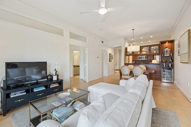 living room with ceiling fan, ornamental molding, beverage cooler, and light hardwood / wood-style floors