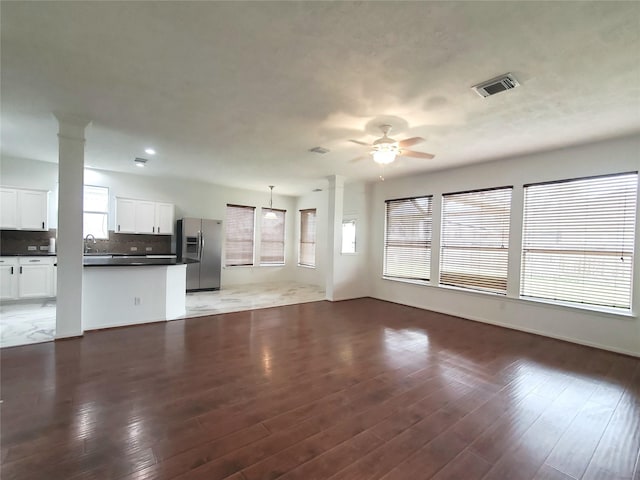 unfurnished living room featuring sink, dark wood-type flooring, ceiling fan, and ornate columns