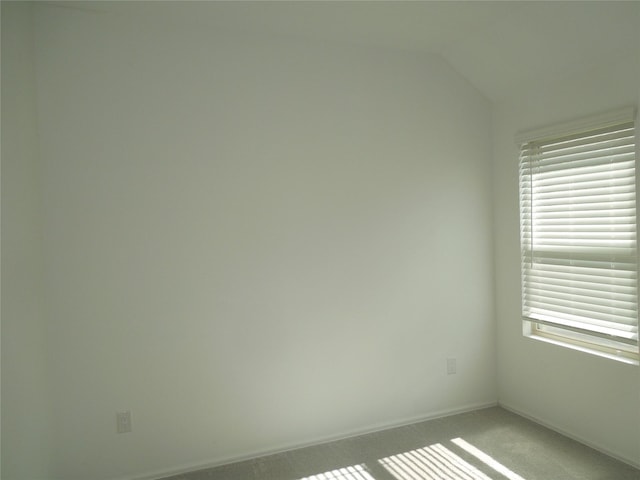 empty room with carpet flooring, baseboards, and vaulted ceiling