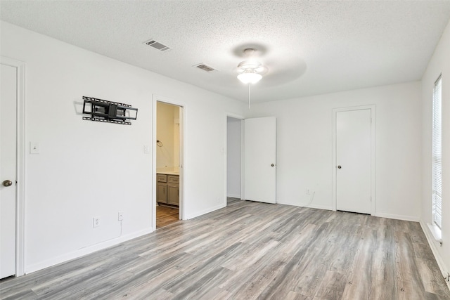 unfurnished bedroom with ensuite bath, multiple windows, ceiling fan, a textured ceiling, and light wood-type flooring