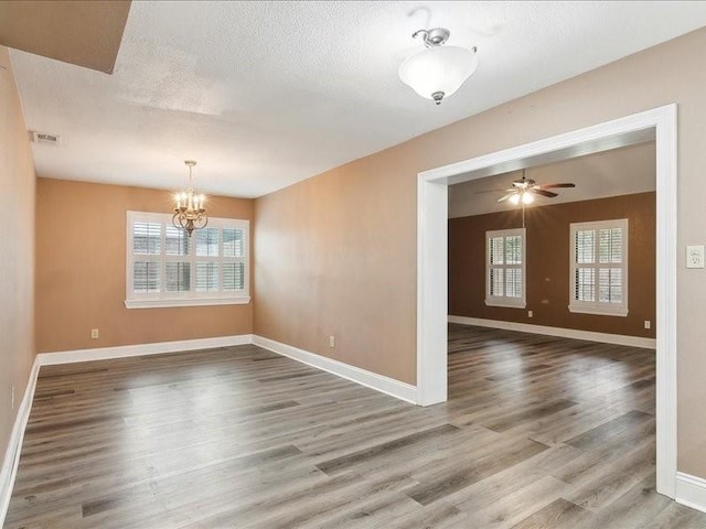 spare room with hardwood / wood-style flooring, plenty of natural light, ceiling fan with notable chandelier, and a textured ceiling