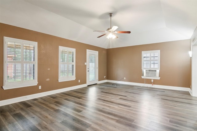 empty room featuring vaulted ceiling, hardwood / wood-style floors, cooling unit, ceiling fan, and a tray ceiling