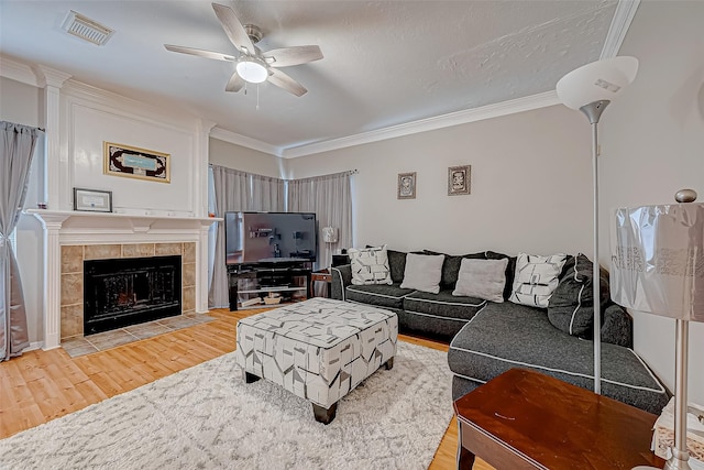 living room featuring hardwood / wood-style flooring, crown molding, ceiling fan, a textured ceiling, and a tiled fireplace