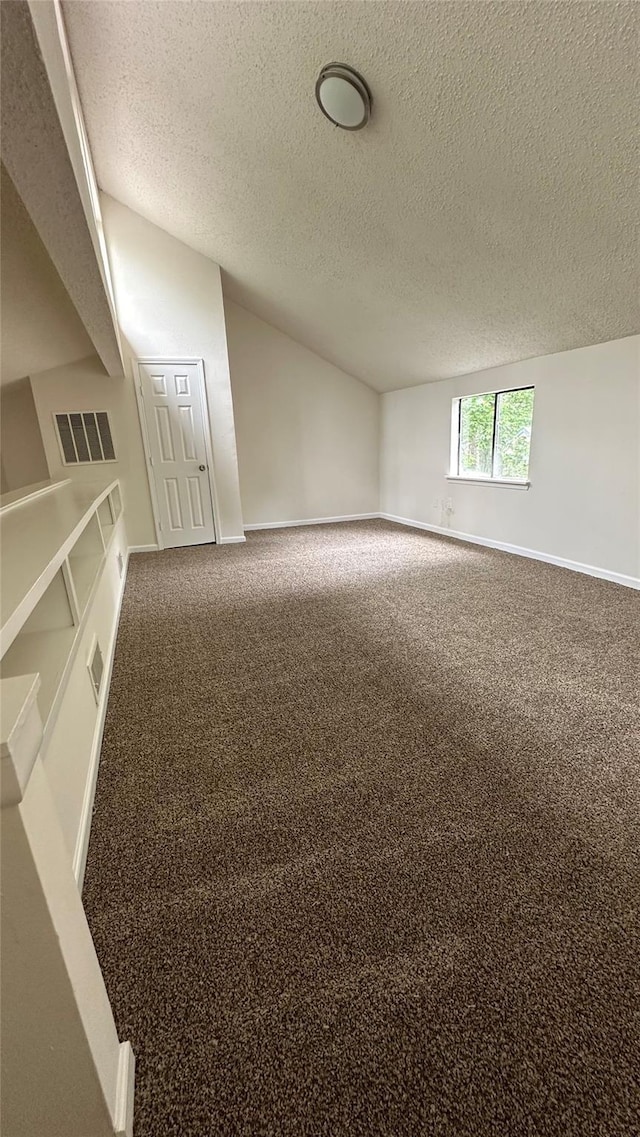 unfurnished room with vaulted ceiling, a textured ceiling, and carpet flooring