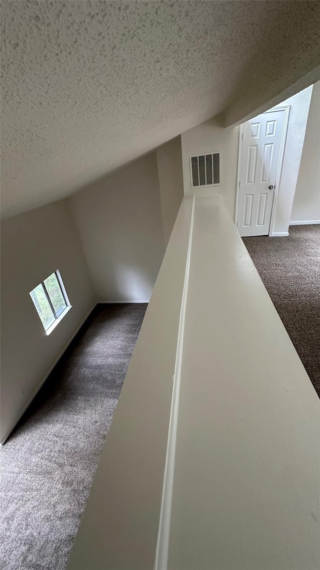 interior space featuring lofted ceiling, a textured ceiling, and dark carpet