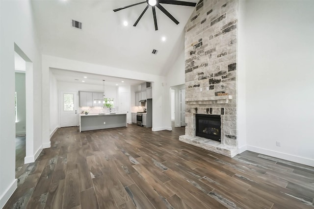 unfurnished living room featuring dark hardwood / wood-style flooring, a stone fireplace, ceiling fan, and high vaulted ceiling