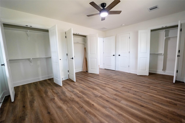 unfurnished bedroom with dark wood-type flooring, ceiling fan, and two closets