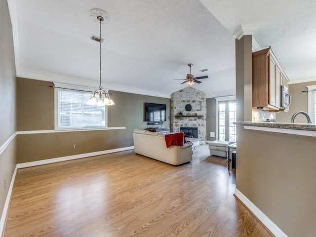 living room featuring sink, ceiling fan with notable chandelier, ornamental molding, light hardwood / wood-style floors, and a stone fireplace