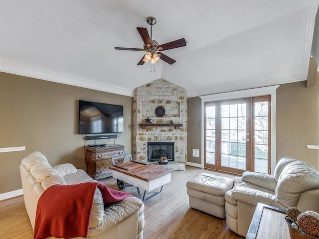 living room featuring vaulted ceiling, a stone fireplace, crown molding, and light wood-type flooring