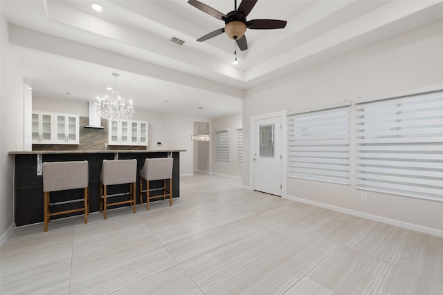 living room with ceiling fan with notable chandelier, a raised ceiling, and light tile patterned flooring