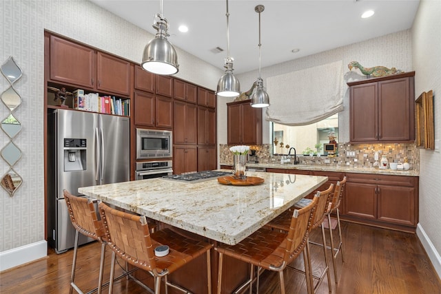 kitchen with pendant lighting, appliances with stainless steel finishes, light stone counters, a kitchen island, and dark hardwood / wood-style flooring