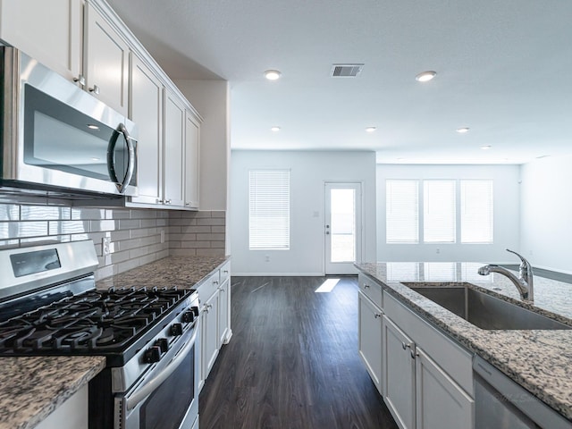 kitchen with sink, white cabinetry, light stone counters, stainless steel appliances, and backsplash