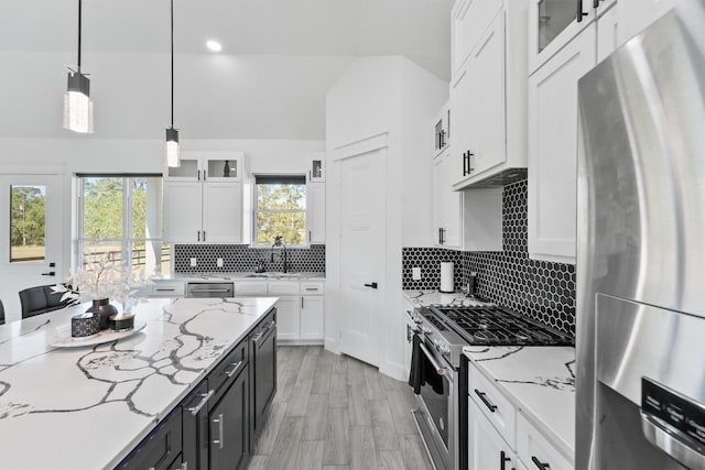 kitchen featuring pendant lighting, appliances with stainless steel finishes, light stone countertops, a healthy amount of sunlight, and white cabinets