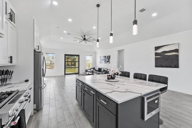 kitchen featuring white cabinetry, light stone counters, decorative light fixtures, appliances with stainless steel finishes, and a kitchen island