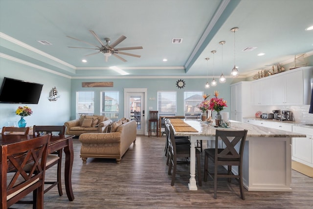 dining area with a raised ceiling, ornamental molding, dark wood-type flooring, and ceiling fan