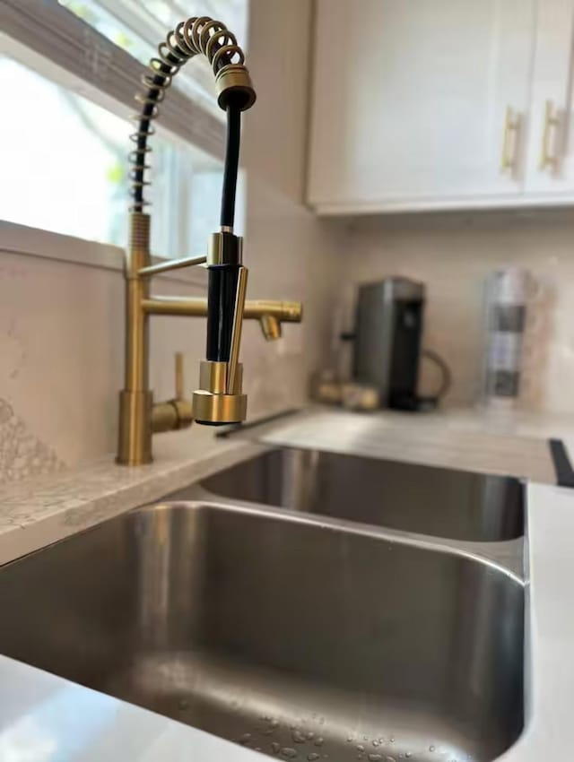 room details featuring white cabinetry, sink, and light stone counters