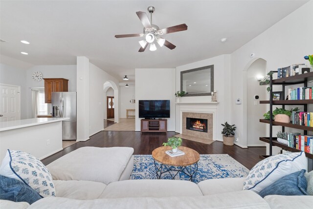 living room with dark wood-type flooring, ceiling fan, and a tile fireplace