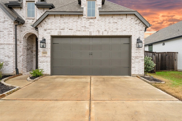 garage at dusk with concrete driveway and fence