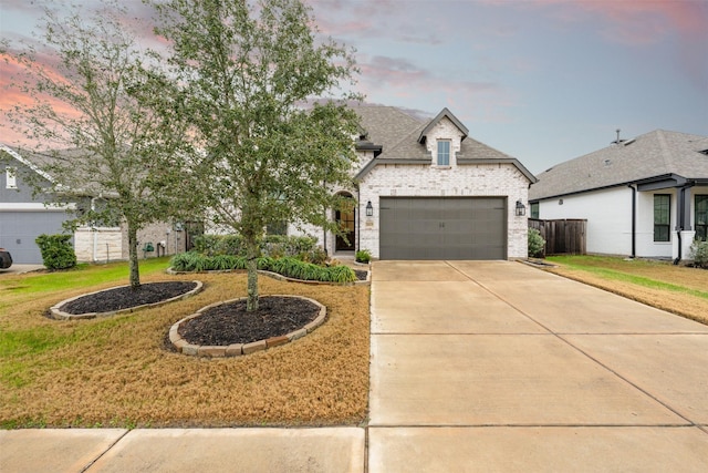 french country style house featuring a yard, brick siding, driveway, and a garage