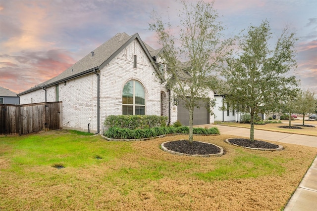 view of front facade with driveway, brick siding, roof with shingles, fence, and a front yard