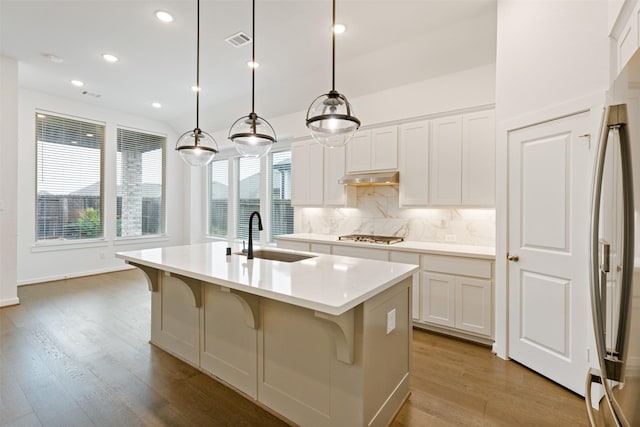 kitchen featuring stainless steel appliances, a sink, visible vents, backsplash, and an island with sink