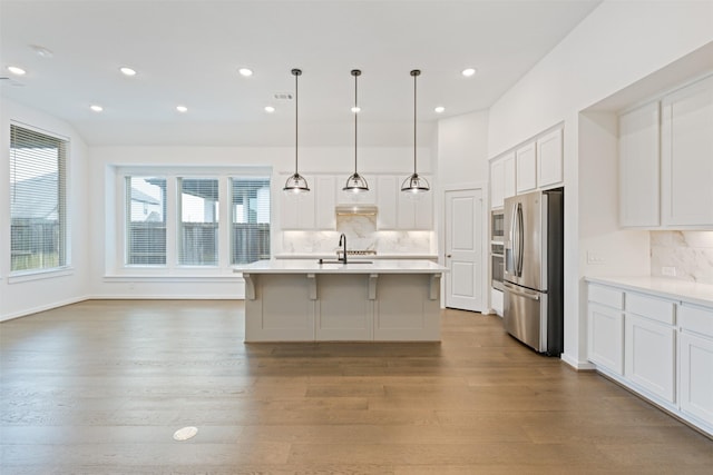 kitchen with white cabinets, stainless steel fridge with ice dispenser, wood finished floors, light countertops, and a sink