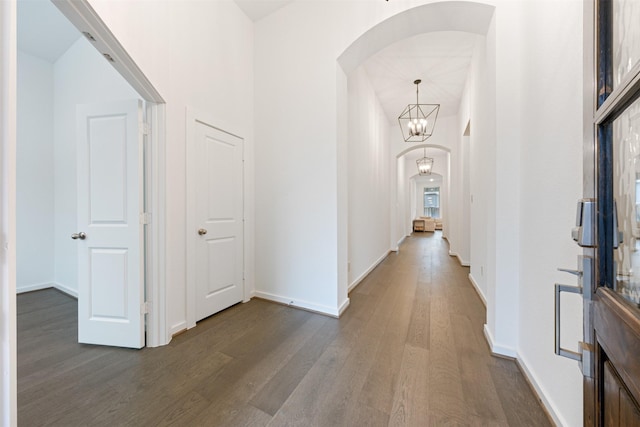 hall with dark wood-style floors, arched walkways, baseboards, and an inviting chandelier