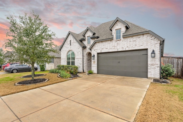 french country style house with concrete driveway, brick siding, roof with shingles, and an attached garage