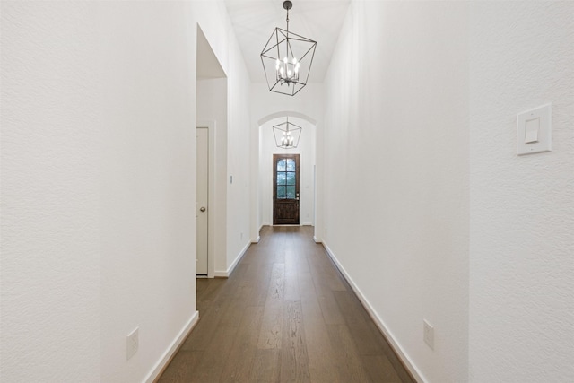 hall featuring an inviting chandelier, baseboards, arched walkways, and dark wood finished floors