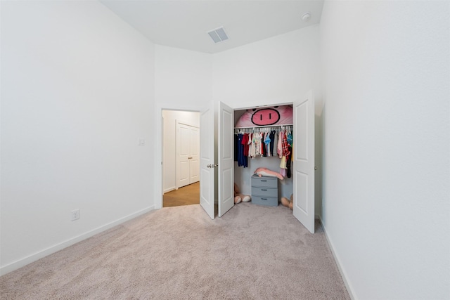 unfurnished bedroom featuring light carpet, baseboards, visible vents, a towering ceiling, and a closet