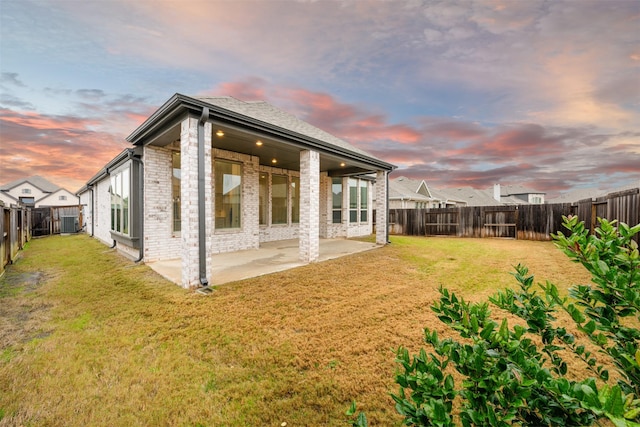 back of property at dusk featuring a yard, a patio area, brick siding, and a fenced backyard