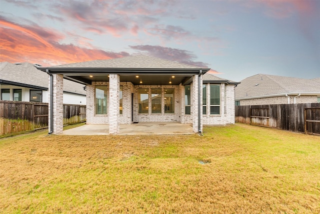 back of property with a patio, brick siding, a lawn, and a fenced backyard