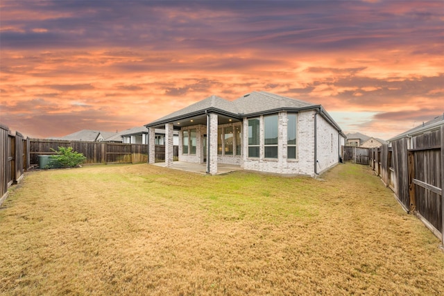 rear view of property with brick siding, a patio, a shingled roof, a lawn, and a fenced backyard