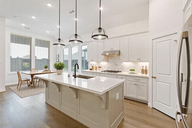 kitchen featuring under cabinet range hood, a sink, visible vents, tasteful backsplash, and stainless steel fridge