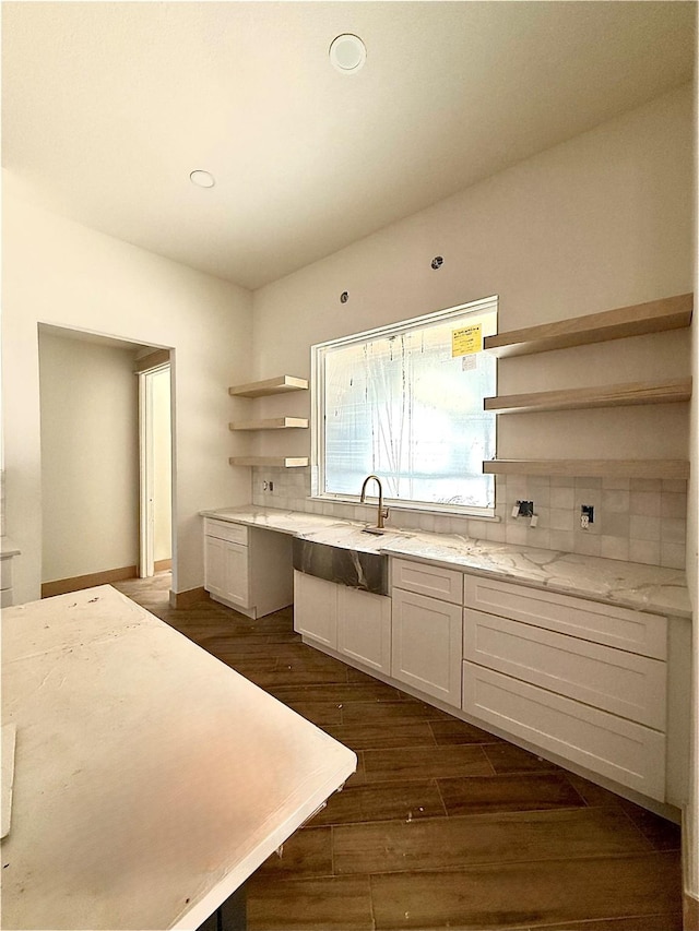 kitchen with sink, white cabinetry, light stone counters, dark hardwood / wood-style floors, and backsplash