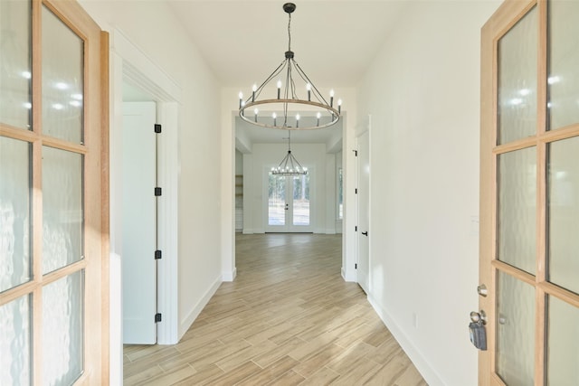 hall featuring light wood-type flooring, french doors, baseboards, and a notable chandelier