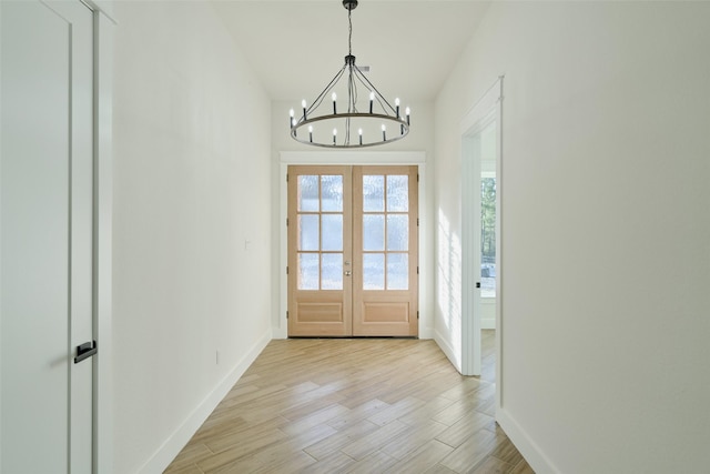 doorway featuring light wood-type flooring, baseboards, a notable chandelier, and french doors